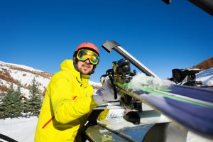 Active man fastening skis on the roof of car