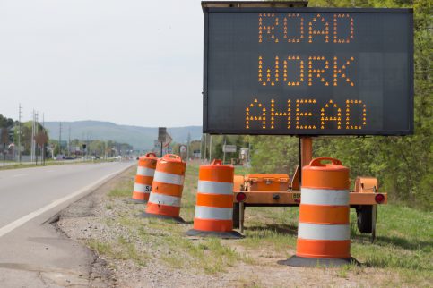 The road cones and lit sign indicate road work ahead. No identifiable commerical signs, cars are in a distance out of focus.