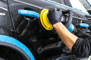 Car polish wax worker hands applying protective tape before polishing. Buffing and polishing car. Car detailing. Man holds a polisher in the hand and polishes the car