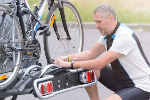 Man wearing sportswear loading bicycles on the bike rack mounted to a car towbar