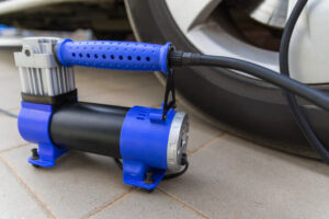 Blue automobile compressor, standing next to the car wheel. Electric air pump inflates the tire, repaired after puncture.