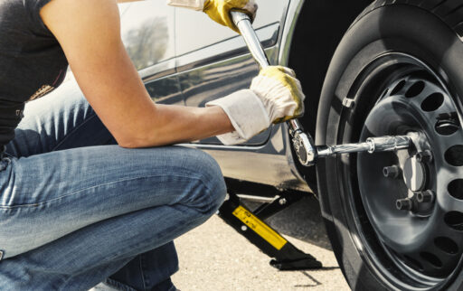 Woman is changing tire of her car with wheel wrench.