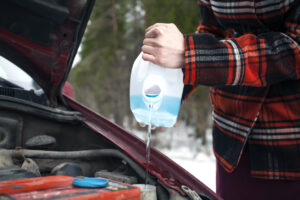 Closeup shot of hands holding bottle with antifreeze washer fluid and pouring it into windshield washer tank in winter day.