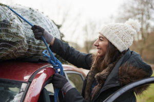 Young woman tying Christmas tree to roof of a car, close up