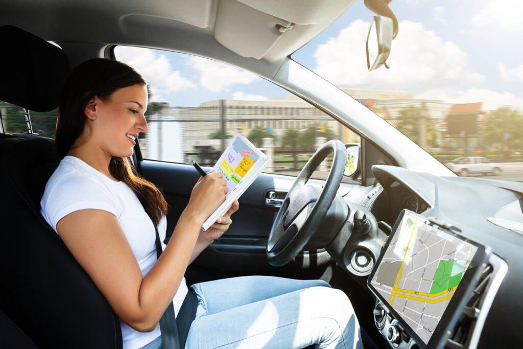 Beautiful Young Woman Sitting Inside Car Writing Schedule In Diary