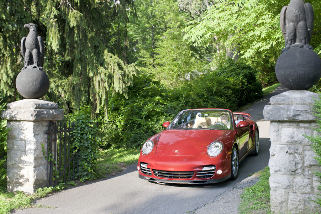 A maroon 997 generation Porsche 911 Turbo convertible being driven down a driveway